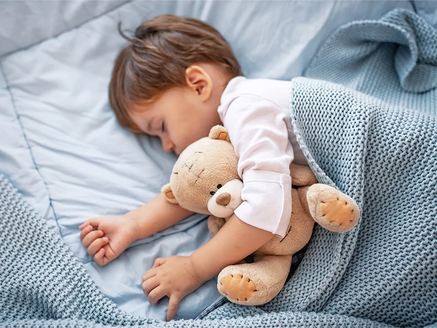 Kind schläft im Bett mit Teddy