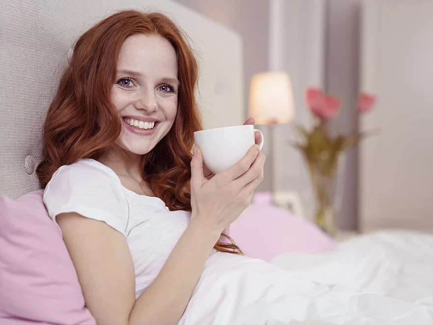 Frau sitzt im Bett mit einer Tasse Tee