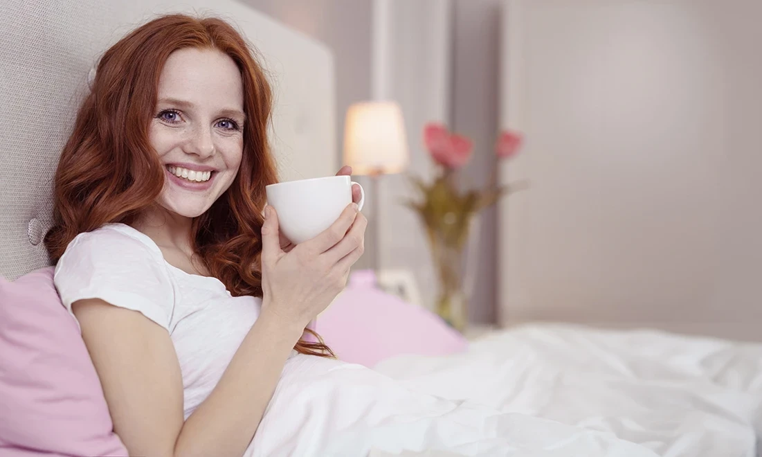 Frau sitzt im Bett mit einer Tasse Tee