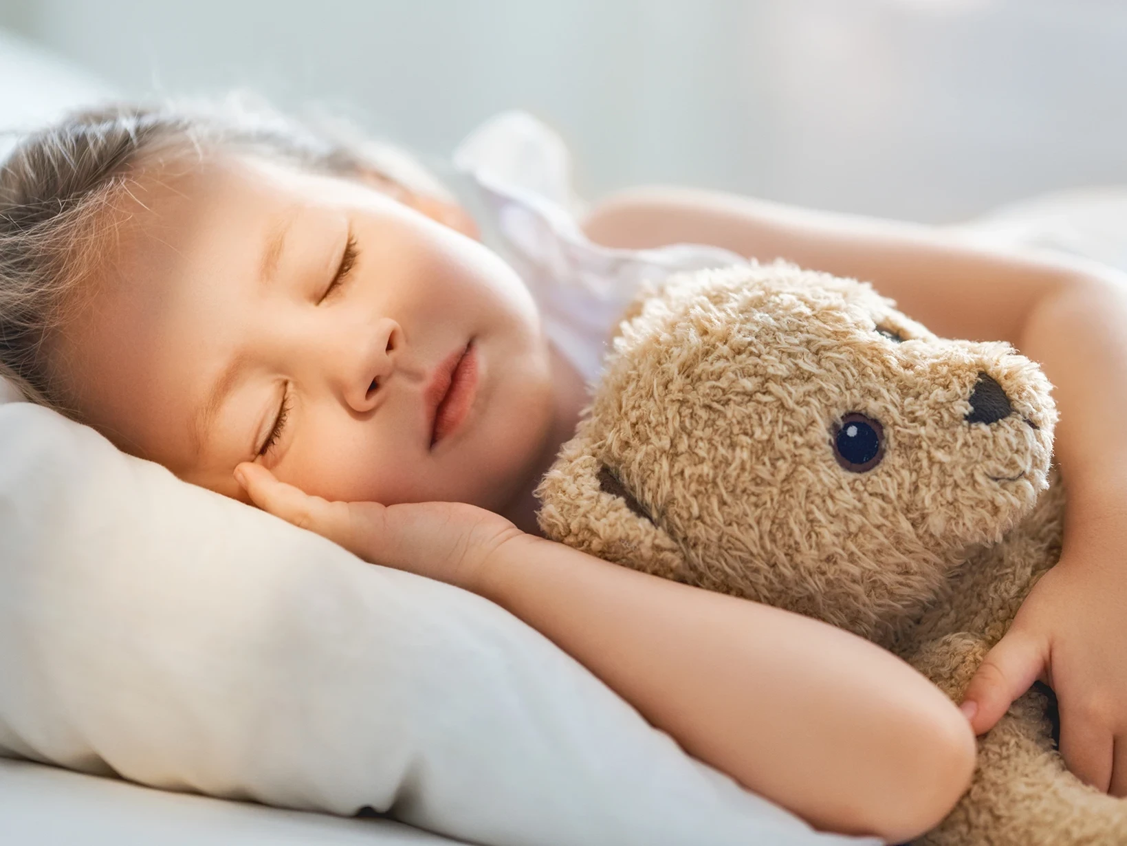 Ein Kind schläft im Bett mit einem Teddybär im Arm