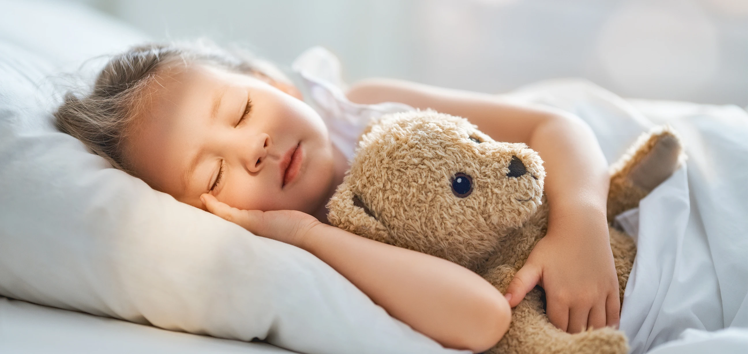 Ein Kind schläft im Bett mit einem Teddybär im Arm